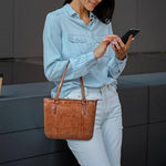Person holding a brown leather handbag and using a smartphone against a neutral background